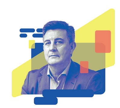 Foto de homem de pele branca e cabelos curtos olha para a câmera seriamente. Ele usa uma camisa clara e um paletó cinza escuro.