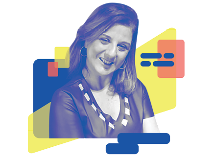 Foto de mulher de pele clara e cabelos lisos na altura do ombro com mechas loiras. Ela está com a cabeça inclinada, sorri e olha para a câmera. Usa brincos de argola e uma blusa preta com gola em V.